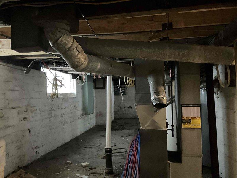 Conducted assessment for HVAC system replacement in three-story home currently using dual furnace setup. Client prefers consolidation to single furnace if feasible. Inspection of basement revealed existing furnace with deteriorating ductwork and inadequate insulation. Third floor will require new ductwork installation. Photos documented current system configuration including metal ductwork, PEX plumbing proximity, and overall mechanical space conditions.