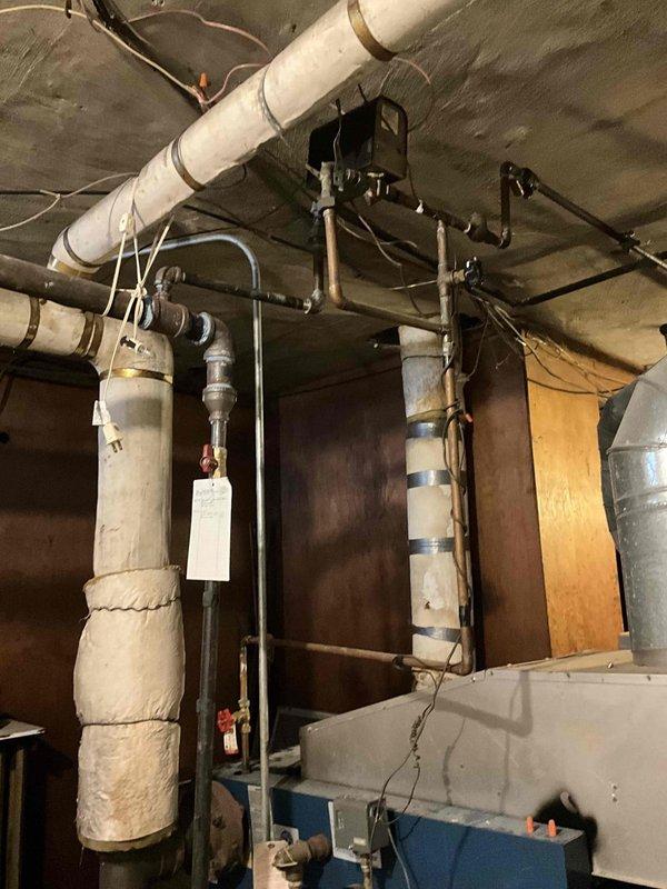 Conducted steam boiler replacement estimate for aged system with deteriorating pipe insulation. Inspection revealed multiple worn components in the mechanical area, including compromised insulation on main vertical and horizontal distribution pipes. Recommendation for complete replacement of existing 2/12 steam boiler with new unit.