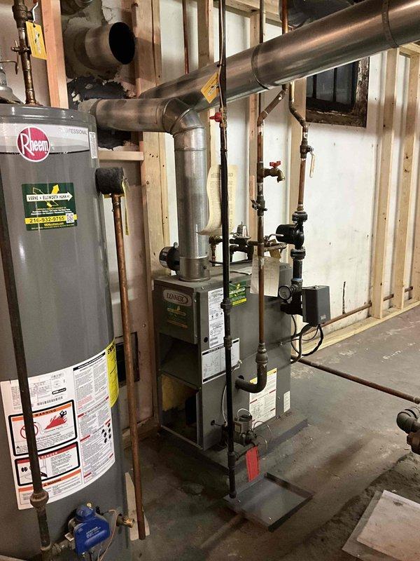 Performed routine maintenance on dual boiler system including thorough brushing to remove soot accumulation and operational cycling test. Inspected wet burner as reported and documented system condition through photographs of the basement mechanical room showing water heater, furnace, and associated ductwork/piping configuration.