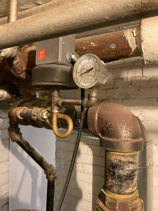 Performed standard boiler tune-up service including application of second dose cleaner. Inspected burner assembly confirming proper flame pattern with characteristic blue flames indicating efficient gas combustion. Checked system pressure gauge and examined plumbing components, noting some oxidation on iron pipes while confirming all connections and valves were functioning correctly.