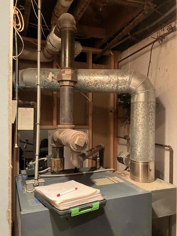 Conducted boiler assessment in residential basement. Inspected existing furnace system with associated ductwork, noting condition of galvanized metal ventilation components and connections. Evaluated circulation pump mounted on wall with connected copper piping for integration with heating infrastructure.