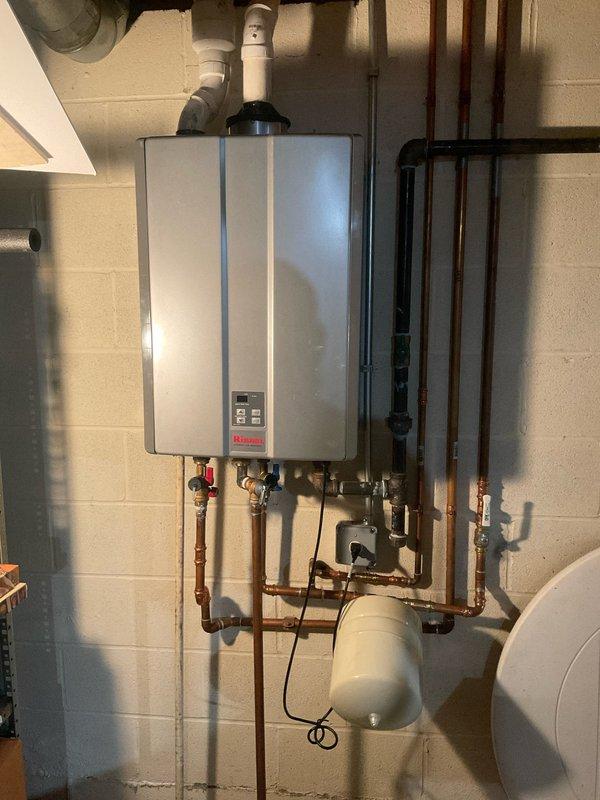 Performed maintenance service on Elvernay tankless water heater in 37-year-old residential property. Inspected unit mounted on concrete block wall, checked all copper and PVC pipe connections, and examined the expansion tank for proper operation. Found and cleaned sump pump basin with accumulated sediment affecting water discharge efficiency, replacing the pump's discharge line to restore proper functionality.