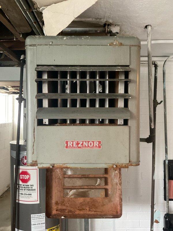 Conducted inspection of aging tanked water heater system with significant corrosion and deterioration evident throughout the installation. Assessment revealed a Reznor unit with extensive rust damage to the lower section, compromised copper components, and potential ventilation issues. Recommended replacement of the 30-gallon water heater due to end-of-life condition and safety concerns.