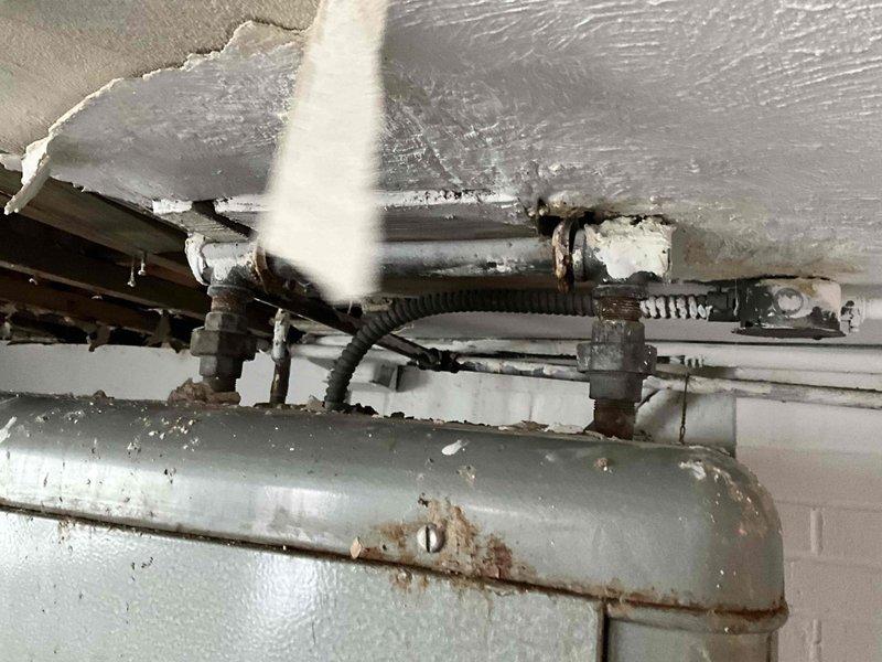 Conducted site assessment of Reznor heater in basement area with significant ceiling damage and deterioration. Identified Lennox HVAC system and adjacent water heater with visible corrosion and aging components. Documented extensive structural issues including exposed joists, crumbling ceiling material, and compromised mechanical installation area requiring full replacement options.