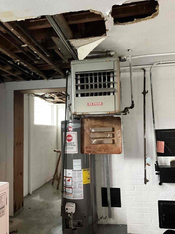 Conducted site assessment of Reznor heater in basement area with significant ceiling damage and deterioration. Identified Lennox HVAC system and adjacent water heater with visible corrosion and aging components. Documented extensive structural issues including exposed joists, crumbling ceiling material, and compromised mechanical installation area requiring full replacement options.