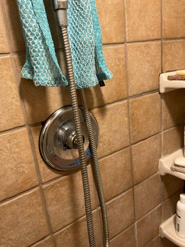 Inspected shower faucet shut-off issue via wall access panel. Assessed control valve and associated plumbing components behind wall, revealing insulation material around the valve assembly. Evaluated the shower control valve, flexible metal hose connection, and surrounding tile integrity to diagnose shut-off malfunction.