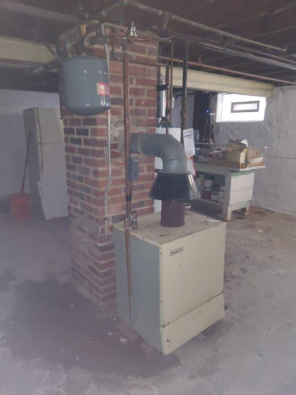 Performed second opinion evaluation on 30+ year old boiler system after previous repair resulted in leakage. Inspection revealed aging installation with standard expansion tank mounted on brick chimney structure and copper distribution piping. Richmond "INTEGRA" water heater with 8-year warranty also present in utility area, appearing in functional condition with no visible issues. Recommended comprehensive assessment of pressure relief valve and system components to address ongoing leakage concerns.