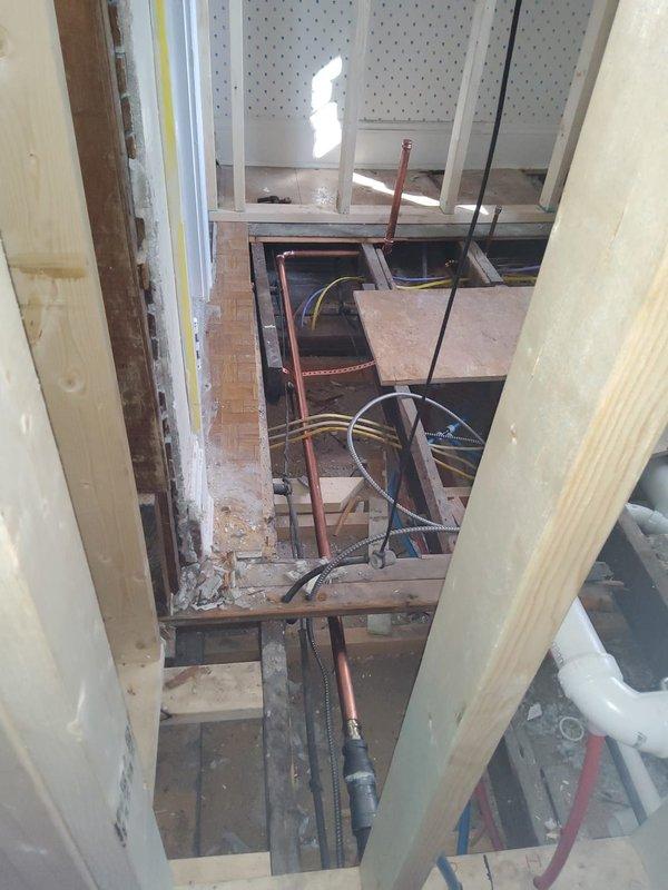 Completed initial phase of multi-stage steam radiator relocation project, removing and preparing to reinstall two radiators from 2nd floor bedroom and 3rd floor bathroom to adjacent rooms. Accessed and evaluated concealed steam line in wall between dining room and kitchen, requiring further assessment once demolition is complete. Relocated cooling thermostat in dining room to adjacent wall and documented exposed subfloor structure and ceiling cavity to prepare for subsequent pipe modifications.