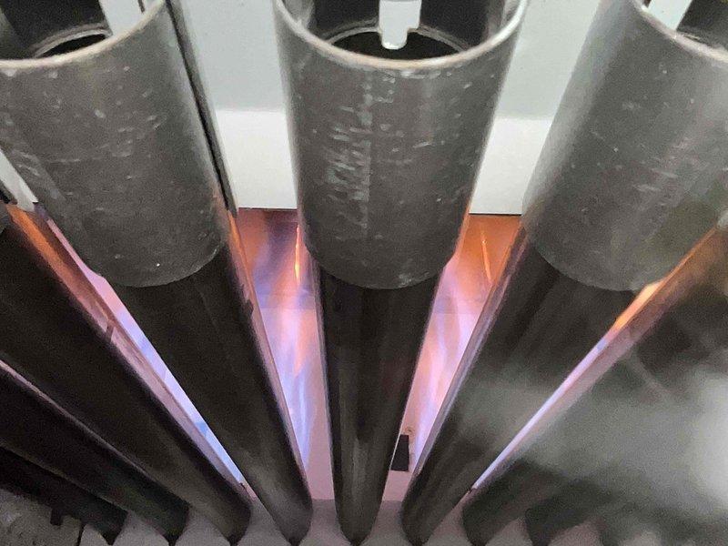 Completed Home Plan Heating Tune Up service on a gas furnace system. Inspected burner assembly showing proper blue-to-orange flame pattern indicating efficient combustion, though minor sooting was observed on upper portions of burner tubes. Examined heat exchanger which displayed normal aging with some dust accumulation but remains in functional condition with no significant corrosion or damage detected.