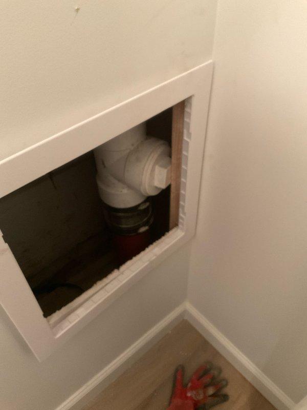 Responded to service call for toilet and drain backup issues causing gurgling. Accessed main drain cleanout point through wall panel to inspect PVC drain pipe connections. Observed significant water damage and possible mold growth around utility sink area, indicating chronic drainage problems that were likely contributing to the backup situation.