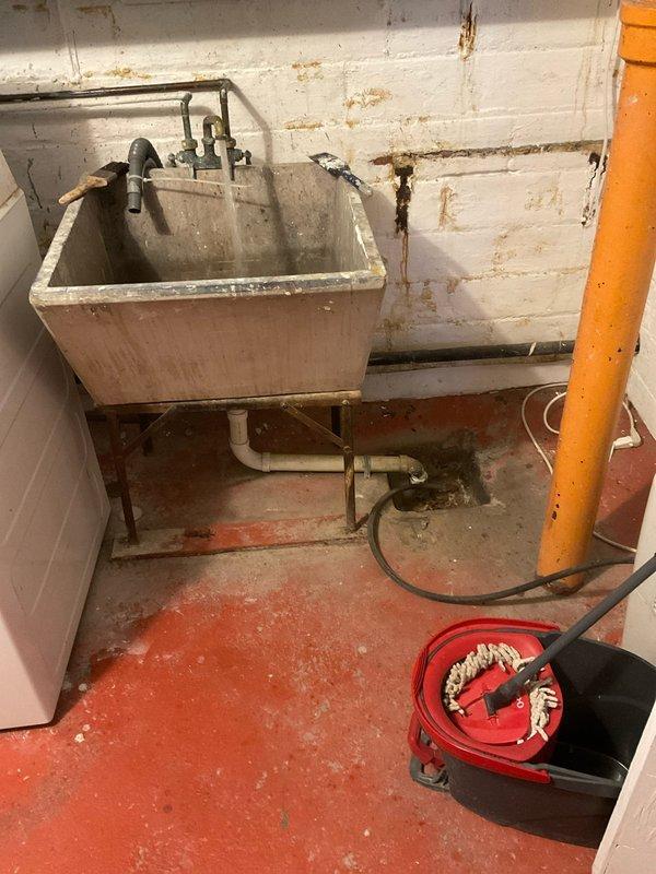 Responded to service call for toilet and drain backup issues causing gurgling. Accessed main drain cleanout point through wall panel to inspect PVC drain pipe connections. Observed significant water damage and possible mold growth around utility sink area, indicating chronic drainage problems that were likely contributing to the backup situation.