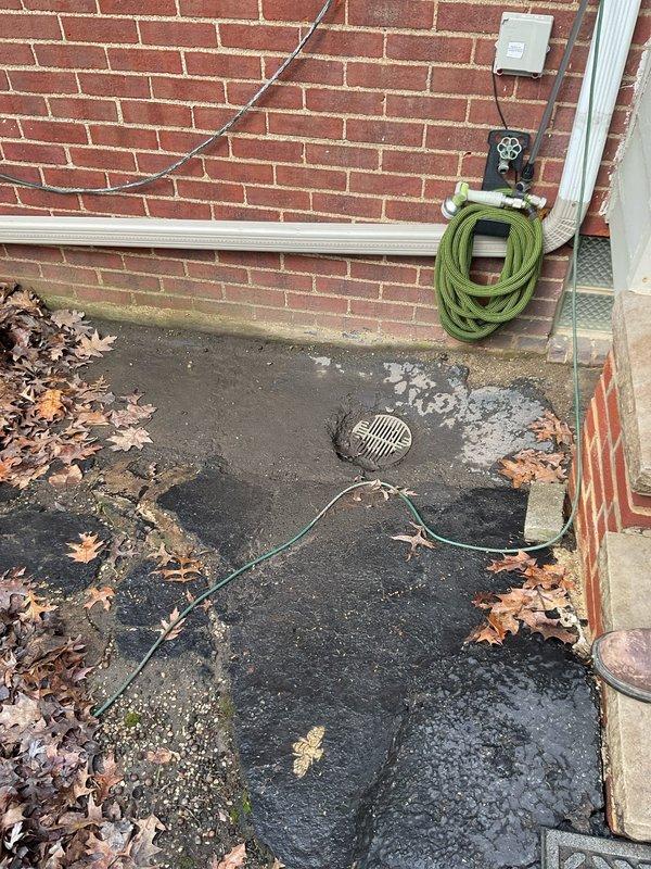 Responded to customer complaint of water backing up near house foundation. Inspection revealed multiple drain openings with significant deterioration, including a circular drain surrounded by cracked concrete with damage radiating outward. Cleared debris from drains and removed accumulated leaves to restore proper drainage functionality and prevent further water accumulation near the structure.