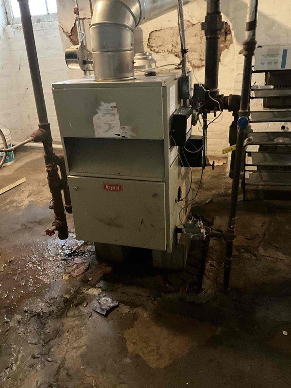 Conducted boiler inspection at residence with reported no heat issue. System evaluation revealed an aging Bryant steam boiler in poor condition (rated 3/10) with evidence of substantial water damage to surrounding area, peeling wall paint, and moisture on concrete floor. Recommended full replacement due to deteriorated condition and inefficient operation.