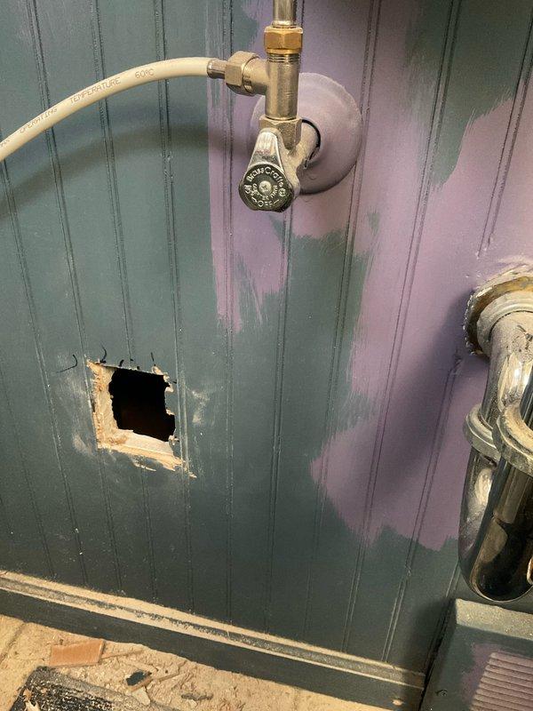 Responded to service call for a customer-drilled hot water pipe. Upon inspection, found damage to copper hot water line behind teal/green beadboard wall. Cut access panel, replaced damaged section of pipe, and installed new shutoff valve with flexible supply line. Tested system for proper function and pressure.