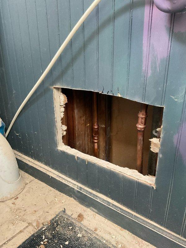 Responded to service call for a customer-drilled hot water pipe. Upon inspection, found damage to copper hot water line behind teal/green beadboard wall. Cut access panel, replaced damaged section of pipe, and installed new shutoff valve with flexible supply line. Tested system for proper function and pressure.