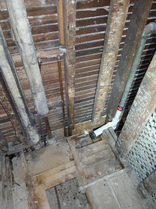 Accessed interior wall by creating opening to expose existing shower drain wye fitting. Removed old wye and installed new PVC wye with 2" drain for shower, including cap for bath authority's future shower stall installation. Completed all necessary plumbing connections through existing wooden framework while working around multiple existing pipe systems.