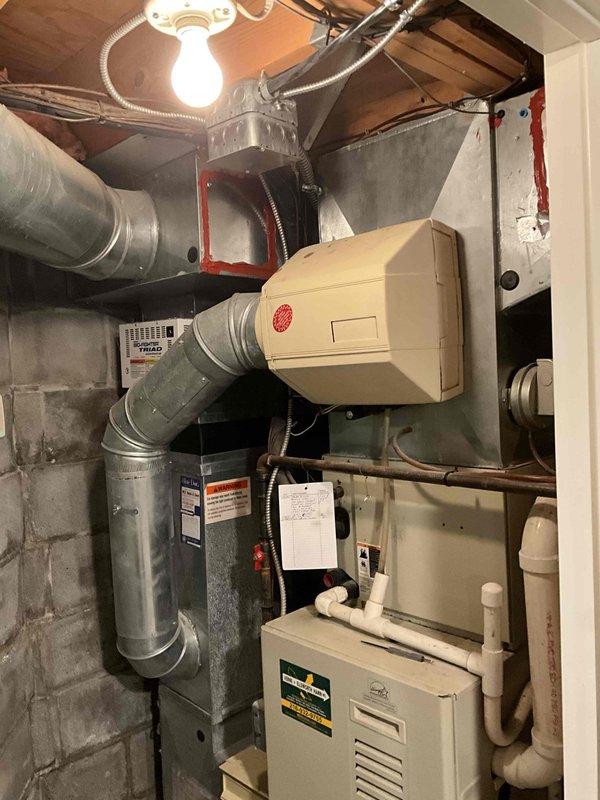 Conducted site assessment for replacement of two existing AC units with heat pump systems to create a hybrid heating solution. Exterior inspection revealed two condenser units (cylindrical and box-shaped) positioned alongside concrete walkway near residential building. Interior evaluation of mechanical room showed existing furnace system with connected ductwork, air handler, and associated PVC drainage pipes that will be integrated with new heat pump installation for optimal hybrid operation.