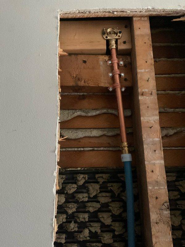 Responded to callback regarding recent hot/cold water nozzle installation. Diagnosed issue where hot water was not flowing when both valves were open, requiring customer to shut off cold water for hot water function. Also addressed newly reported wobble in shower arm connection to wall. Inspection of wall cavity revealed proper copper pipe installation with brass fittings and appropriate securing brackets, requiring adjustment to valve cartridge to resolve water flow issue and tightening of shower arm connection to eliminate movement.