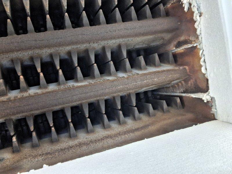 Performed routine heating maintenance inspection. Observed significant rust and corrosion on ventilation grill with poor sealing to surrounding surface. Heat exchanger fins showed dust accumulation requiring cleaning to improve thermal efficiency and system performance.