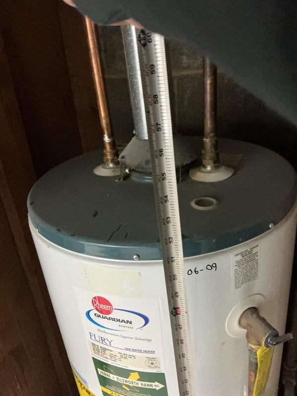 Conducted a follow-up assessment of an aging Rheem Guardian "FURY" water heater installation. Documented existing unit configuration including copper pipe connections, gas line placement, and current venting through brick wall. Photographed the complete system to evaluate replacement options, noting the deteriorating mortar around pipe penetrations and the confined utility space constraints that will impact new unit specifications.