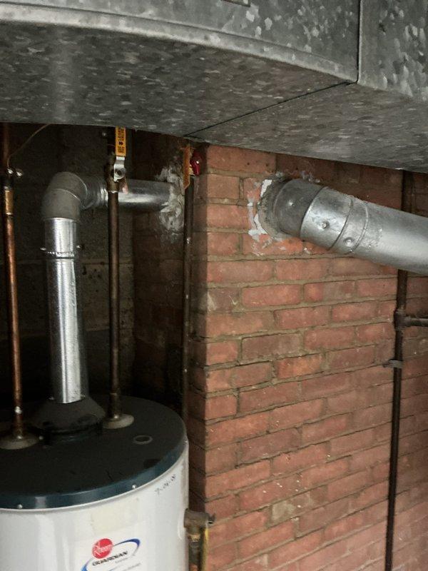 Conducted a follow-up assessment of an aging Rheem Guardian "FURY" water heater installation. Documented existing unit configuration including copper pipe connections, gas line placement, and current venting through brick wall. Photographed the complete system to evaluate replacement options, noting the deteriorating mortar around pipe penetrations and the confined utility space constraints that will impact new unit specifications.