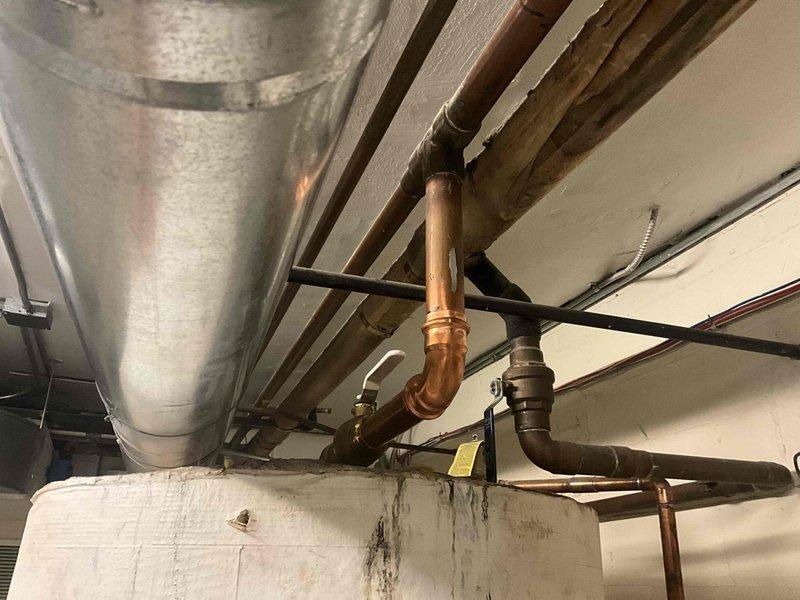 Conducted on-site evaluation for boiler and hot water storage tank replacement. Assessed existing water heater showing signs of base leakage and floor water damage, documented current copper and black iron piping configuration, HVAC ductwork routing, and ventilation system requirements. Photographed equipment specifications, existing connections including braided flex lines and valve assemblies, and structural mounting conditions to provide comprehensive estimate for new boiler system with integrated storage tank installation.