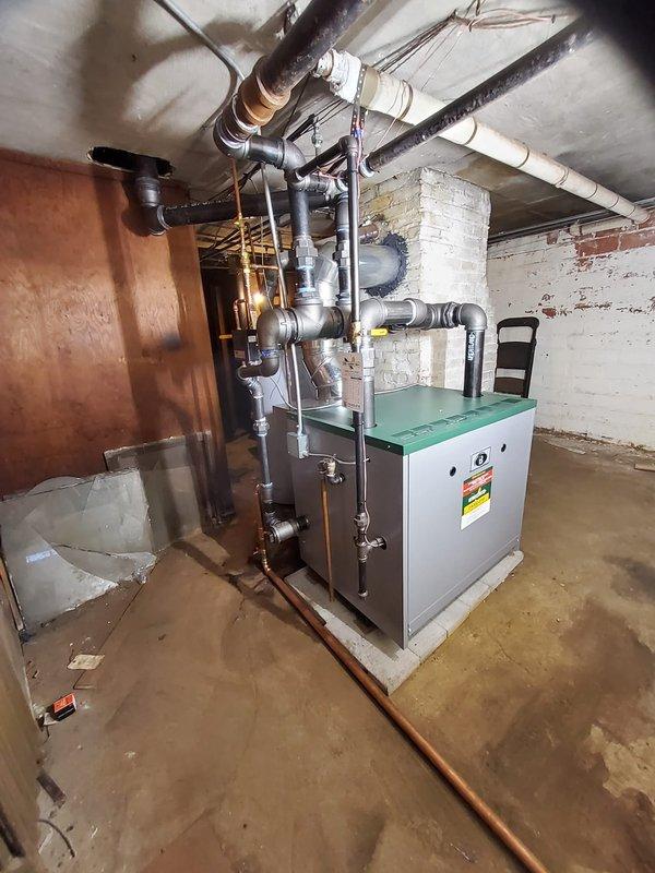 # HVAC Install - Steam Gas Boiler

Completed full steam boiler replacement in vacant residential property under financing arrangement. Coordinated asbestos abatement prior to installation to ensure safe working conditions and regulatory compliance.

Removed existing boiler system and installed new steam gas boiler unit on concrete pad in basement mechanical room. Connected system to existing steam distribution piping using black iron pipe with appropriate fittings and isolation valves. Installed new backflow preventer to protect potable water supply and new automatic water feeder to maintain proper boiler water levels. Configured venting system with metallic ductwork to ensure proper combustion air supply and exhaust ventilation per manufacturer specifications and local codes.

Installed new thermostat and wired to boiler controls for proper system operation. Tested all safety controls including pressure relief valve, low water cutoff, and gas valve operation. Pressurized system, check