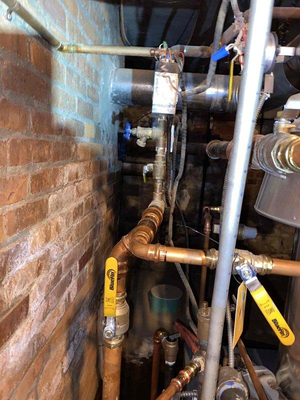 Responded to service call for dripping boiler on one-year-old unit. Upon inspection of the mechanical room, identified minor leak at copper piping connection point near control module. Tightened fitting, verified all valve connections, and confirmed proper operation of boiler system with no further water discharge observed.