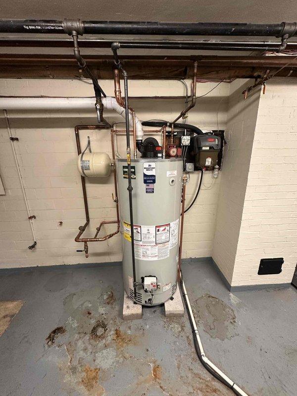 Removed existing boiler system and relocated holding tank to corner of basement utility area. Installed new 75-gallon power vent water heater on concrete platform with proper venting configuration. Connected copper supply lines, installed expansion tank, and completed all electrical conduit runs to code. Unit positioned against concrete block wall with PVC exhaust venting routed through ceiling infrastructure. All plumbing connections pressure tested and verified operational.
