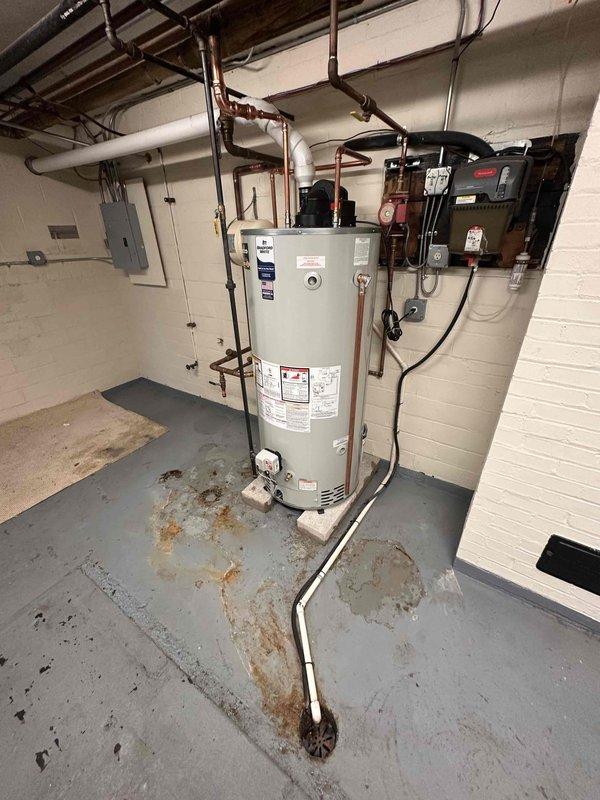 Removed existing boiler system and relocated holding tank to corner of basement utility area. Installed new 75-gallon power vent water heater on concrete platform with proper venting configuration. Connected copper supply lines, installed expansion tank, and completed all electrical conduit runs to code. Unit positioned against concrete block wall with PVC exhaust venting routed through ceiling infrastructure. All plumbing connections pressure tested and verified operational.