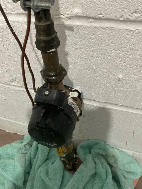 Responded to reported valve leak on plumbing assembly. Upon inspection, identified active leak at valve fitting connection point on wall-mounted system. Placed absorbent material beneath assembly to contain water discharge during evaluation. Assessed valve condition, surrounding pipe connections, and mounting hardware for integrity. Documented existing conditions including mineral deposits and water staining in collection pan, indicating ongoing leak activity. Captured photographic evidence of valve assembly configuration and leak source for service records.