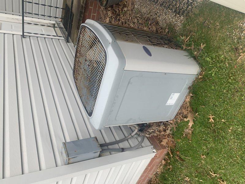 Completed on-site evaluation of 20-year-old residential air conditioning system for replacement estimate. Documented existing outdoor condenser unit mounted on white platform with electrical disconnect box, protective cage enclosure, and associated electrical connections. Photographed equipment condition, installation configuration, and surrounding area to provide comprehensive assessment for system replacement proposal.