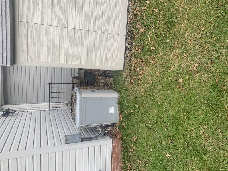 Completed on-site evaluation of 20-year-old residential air conditioning system for replacement estimate. Documented existing outdoor condenser unit mounted on white platform with electrical disconnect box, protective cage enclosure, and associated electrical connections. Photographed equipment condition, installation configuration, and surrounding area to provide comprehensive assessment for system replacement proposal.
