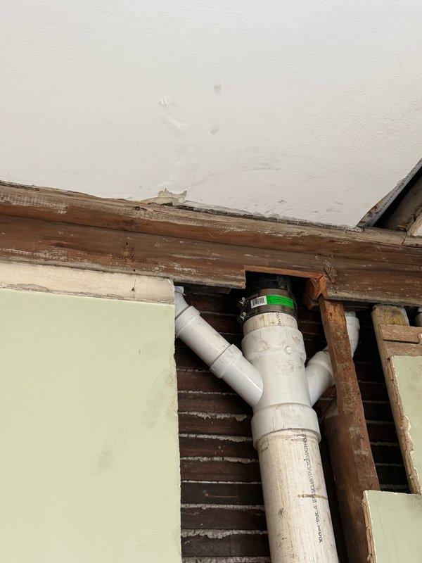 Responded to water leak in ceiling originating from bathroom above previous work area. Upon investigation, identified active leak at PVC drainage pipe connection point near exposed ceiling joists. Accessed affected area through existing opening, inspected plumbing configuration including vertical and angled PVC pipe sections with visible green band marking. Verified leak source at pipe junction, secured connection, and confirmed proper drainage flow. Inspected bathroom fixtures above including toilet and tub area to ensure no additional moisture intrusion points. Documented existing conditions and completed repairs to resolve ceiling leak issue.
