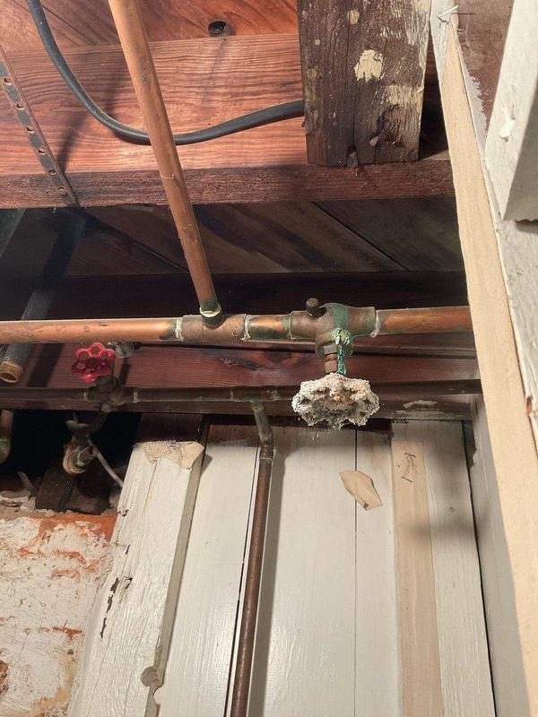 Responded to a plumbing leak in a third-floor bathroom of a 50-year-old home. Upon arrival, documented water damage to ceiling and wall surfaces below the affected area, showing discoloration and moisture staining on drywall and paint. Accessed attic crawl space above bathroom and identified source of leak in aging copper supply line showing significant corrosion and mineral deposit buildup. The corroded section exhibited white crusty accumulation indicating long-term moisture exposure and oxidation. Shut off water supply using existing shutoff valve, removed damaged section of copper piping, and installed new copper pipe section with proper fittings and solder joints. Pressure tested repair to ensure no additional leaks. Advised homeowner that ceiling and wall surfaces will require drying time before cosmetic repairs can be completed, and recommended monitoring for additional plumbing issues given the age of the home's plumbing system and visible oxidation on other copper lines in the