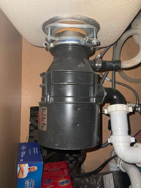 Responded to clogged kitchen sink in 125-year-old home where homeowner was concerned about potential garbage disposal replacement. Upon inspection, found existing black garbage disposal unit with connected dishwasher drain line and standard P-trap configuration beneath single-basin stainless steel sink. Assessed disposal functionality, cleared blockage from drain system, and verified proper drainage flow. Determined existing disposal unit was operational and did not require replacement at this time.