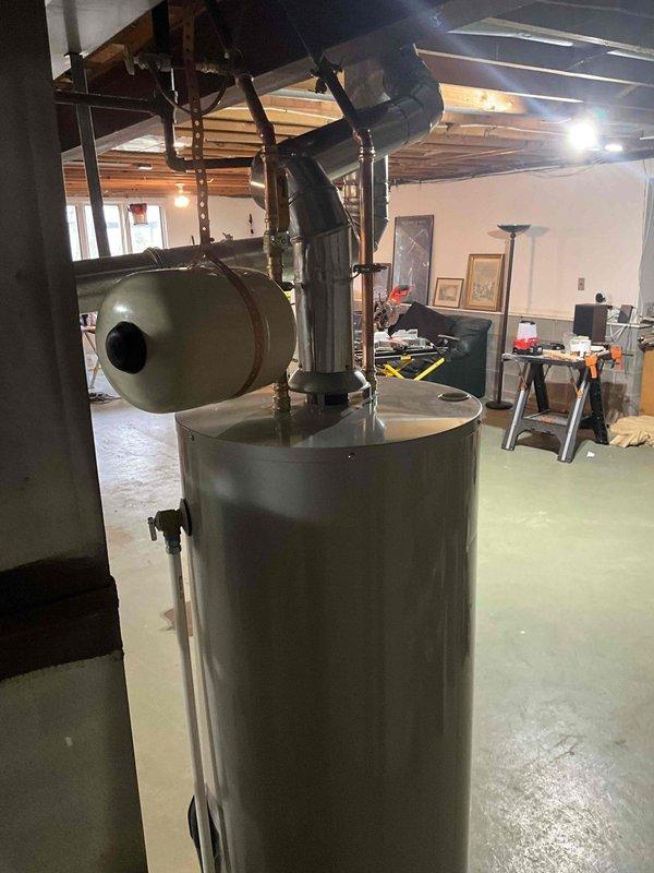 Completed installation of new tanked water heater in basement utility room. Positioned unit on concrete floor with proper clearances and connected copper supply lines with brass fittings to top of tank. Installed venting ductwork extending to ceiling joists and mounted control panel/thermostat on adjacent concrete block wall for temperature regulation. Collected deposit payment as customer approved hot water tank replacement option.