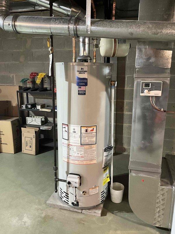 Completed installation of new tanked water heater in basement utility room. Positioned unit on concrete floor with proper clearances and connected copper supply lines with brass fittings to top of tank. Installed venting ductwork extending to ceiling joists and mounted control panel/thermostat on adjacent concrete block wall for temperature regulation. Collected deposit payment as customer approved hot water tank replacement option.
