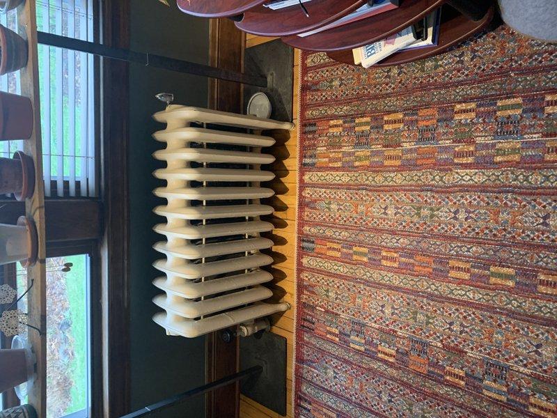 Conducted on-site assessment of residential steam heating system to evaluate cast iron radiator requiring replacement. Inspected vintage multi-column radiator located beneath staircase, documenting existing unit configuration, mounting hardware, and connection points. Evaluated radiator condition noting surface wear and age-related deterioration. Photographed installation area including clearances, piping connections, and surrounding space constraints for accurate replacement specifications. Prepared comprehensive quote for radiator replacement including removal of existing unit and installation of new component compatible with current steam boiler system.