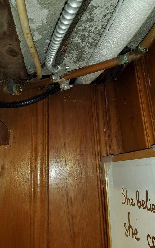 Responded to water leak concern at exterior panels suspected to originate from AC condensate drainage system. Upon inspection, discovered significant water damage and deterioration in basement/crawl space area with compromised wall surfaces, peeling paint, and exposed brickwork. Examined PVC drainage pipes, condensate lines, and associated plumbing infrastructure running along walls and overhead. Documented existing conditions showing white stone drainage bed with debris accumulation, multiple pipe runs including insulated refrigerant lines, copper piping, and flexible conduit installations. Assessed integrity of condensate drain system and mounting hardware. Photographed deteriorated wall conditions, pipe routing, and overhead utility infrastructure for documentation purposes.