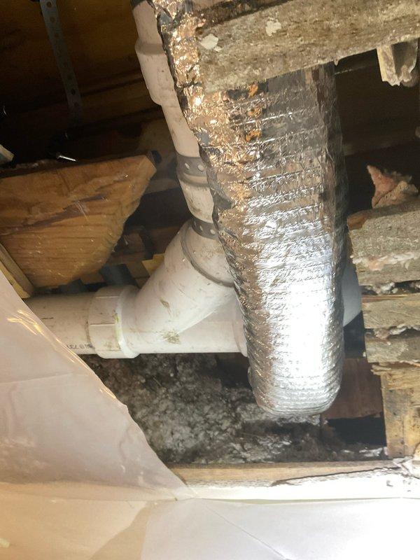 Responded to warranty call for brown water dripping from newly installed plumbing in toddler's bathroom from previous incomplete stacked job. Inspected attic space above bathroom and documented HVAC ductwork, insulation, and plumbing connections. Identified roof leak as source of water intrusion affecting new pipe installation. Photographed affected areas showing flexible aluminum ductwork, PVC pipe connections, exposed framing, and pink fiberglass insulation with visible moisture damage and debris accumulation. Plastic vapor barrier requires re-securing upon completion of repairs.