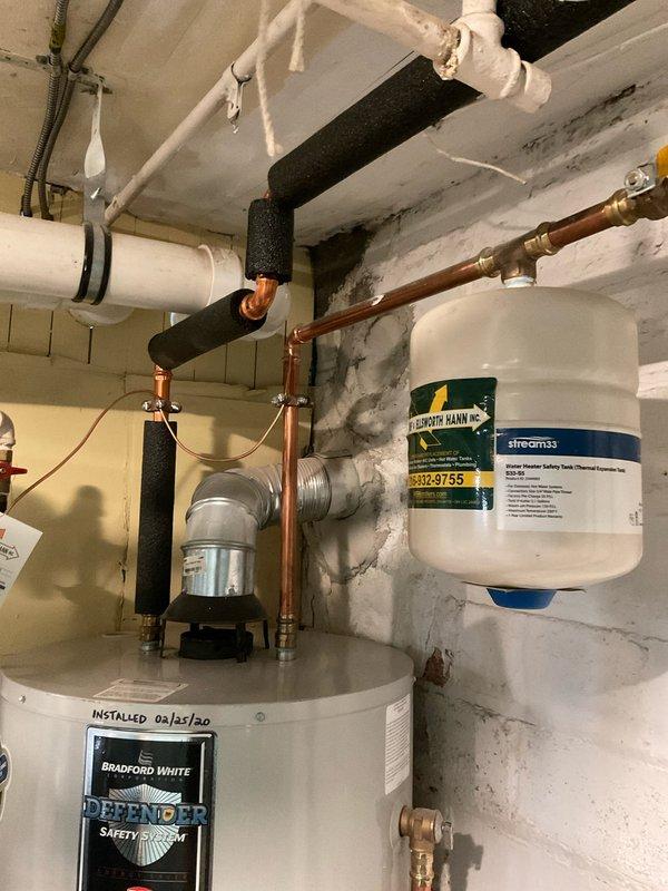 Responded to no hot water complaint at 100-year-old residence with 6-year-old Bradford White water heater installed in March 2020. Upon arrival, performed diagnostic assessment of tanked water heater system including inspection of gas control valve assembly, thermocouple, pilot light operation, and burner functionality. Verified proper operation of copper supply and discharge piping, expansion tank mounted above unit, and isolation valves with yellow handles. Checked drain pan positioning and inspected all visible connections for leaks or corrosion. Tested temperature and pressure relief valve operation and confirmed proper venting configuration. Evaluated water treatment system (Streamax unit) mounted on wall to ensure adequate flow and filtration not impacting heater performance. Inspected gas supply line and control box at base of unit for proper operation. Reset pilot light and verified ignition sequence, confirming burner assembly fired correctly and water heating resumed normal o
