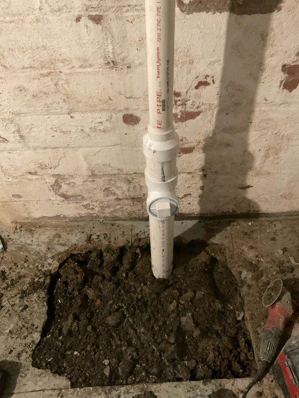 Removed deteriorated cast iron 90-degree bend at connection point to clay piping by breaking up basement concrete floor. Excavated and exposed the damaged fitting, then removed the compromised cast iron section. Installed Schedule 40 PVC piping with cleanout fitting to replace the failed cast iron assembly. Repatched the concrete floor sections that were removed during excavation to restore the surface.
