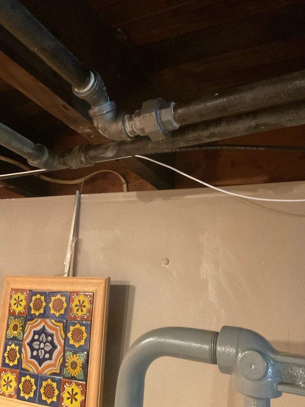 Responded to emergency service call for damaged pipe located above gas meter that had rendered the gas line inoperable. Upon inspection, identified compromised galvanized pipe section with threaded connections in basement utility area requiring immediate replacement. Removed deteriorated pipe segment and installed new pipe section with proper fittings and connections to restore gas line functionality. Verified all joints were properly sealed and tested system integrity to ensure safe operation. Documented existing plumbing configuration including mixed galvanized metal and PVC piping running along exposed wooden joists before completing repairs.