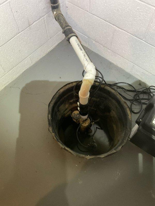 Performed comprehensive sump pump inspection at residential property built in 1993. Evaluated existing sump pump system including basin, discharge piping, and backup battery power supply unit. Assessed pump functionality, electrical connections, and PVC discharge line configuration. System components including black backup power unit with wall-mounted control panel were inspected for proper operation. Verified basin water level management and confirmed all electrical connections were secure and functioning correctly.