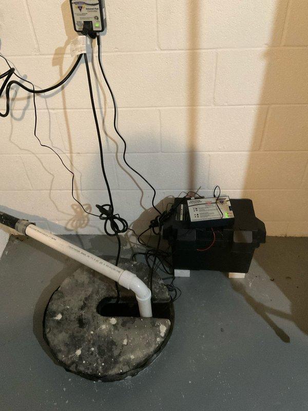 Performed comprehensive sump pump inspection at residential property built in 1993. Evaluated existing sump pump system including basin, discharge piping, and backup battery power supply unit. Assessed pump functionality, electrical connections, and PVC discharge line configuration. System components including black backup power unit with wall-mounted control panel were inspected for proper operation. Verified basin water level management and confirmed all electrical connections were secure and functioning correctly.