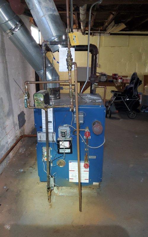 Responded to no heat call on residential boiler system. Upon arrival, found blue cabinet boiler unit in basement with complex piping configuration including copper supply and return lines, expansion tank, and PVC condensate drainage. Performed diagnostic inspection of boiler components including control board, pressure gauges, and safety devices. Verified gas supply, checked electrical connections, and tested ignition sequence. Inspected venting system and condensate drain for proper operation. System restored to normal heating operation. All safety controls verified functional before departure.