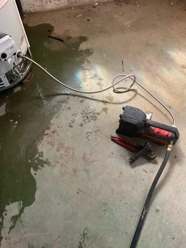 Responded to water heater failure resulting in significant basement flooding. Upon arrival, found extensive water accumulation on concrete floor with dark staining indicating prolonged moisture exposure. Deployed portable vacuum pump with drainage hoses to extract standing water from affected area. Connected discharge lines to floor drain for proper water removal. Coordinated with HVAC technician scheduled for same-day service to address air conditioning system following water heater assessment. Water heater exhibited signs of tank failure requiring immediate attention to prevent further flooding damage.