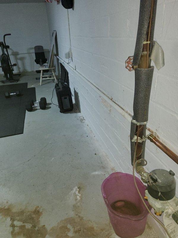 Responded to water leak at return line joint that was recently replaced. Upon arrival, found active leak at pipe connection with bucket positioned to catch dripping water and visible floor staining indicating ongoing moisture issue. Inspected joint connection on copper return line where it meets insulated vertical pipe assembly. Repaired leaking joint by properly sealing and securing the connection point to eliminate water discharge. Verified repair held pressure and no further leakage was present upon completion.