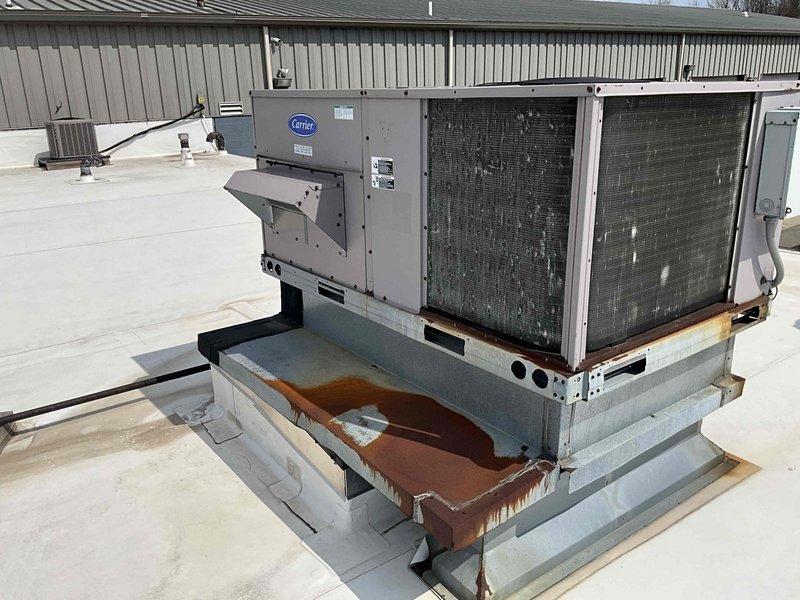 Conducted rooftop estimate for commercial HVAC unit replacement and assessment of two tube heaters. Documented existing Carrier package unit condition, noting significant rust staining on concrete platform and curb adapter, and reviewed installation specifications including mounting requirements, clearances, and equipment weights for proper system sizing and replacement planning.